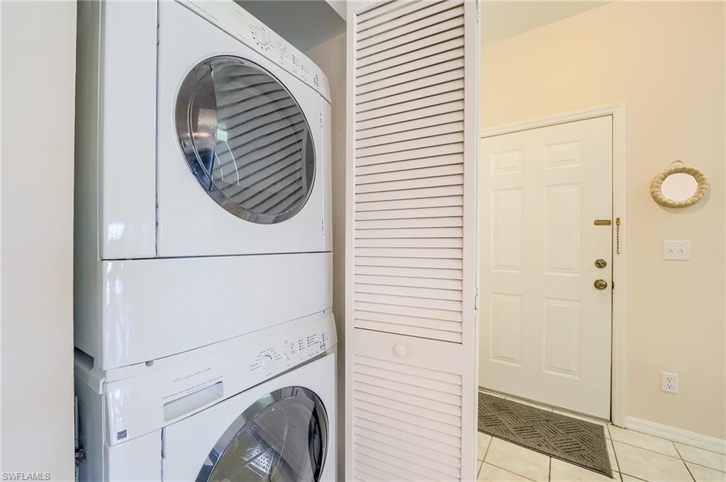 Clothes washing area with stacked washing maching and dryer and light tile patterned floors