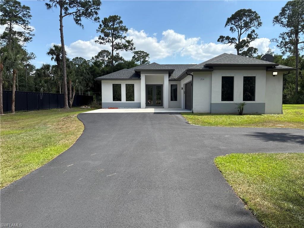 Prairie-style home with a front lawn, aphalt driveway, french doors, fence, and stucco siding