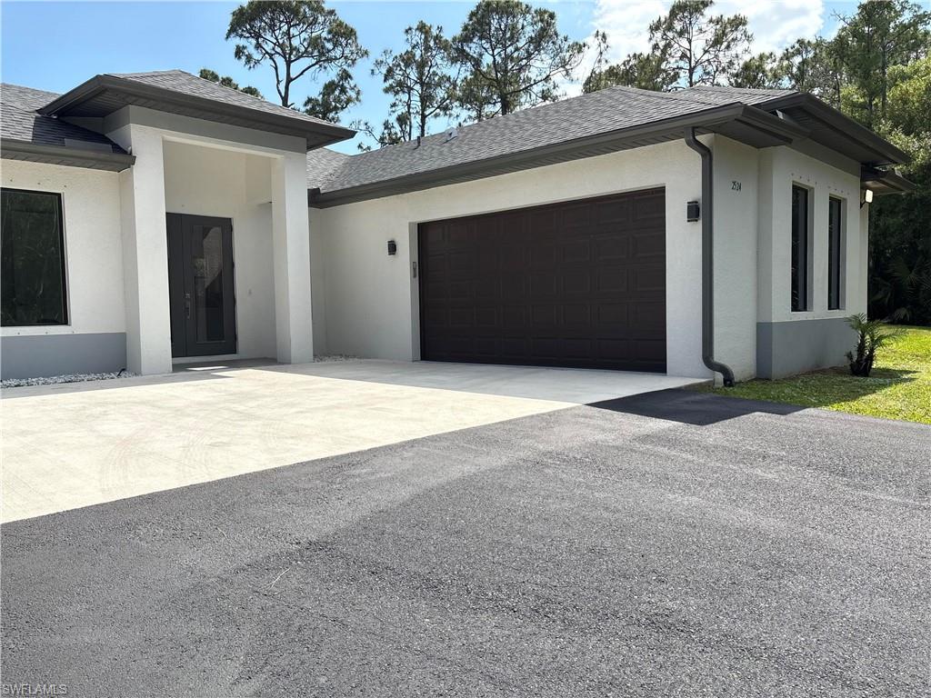View of front facade with stucco siding, roof with shingles, driveway, and a garage