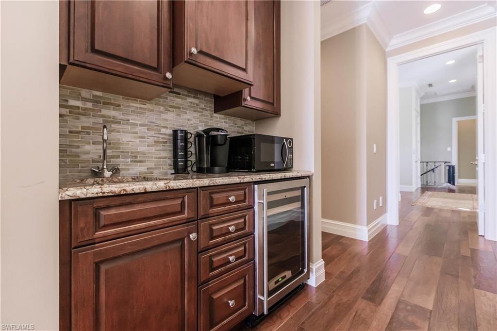 Bar with dark wood-type flooring, wine cooler, tasteful backsplash, light stone countertops, and ornamental molding