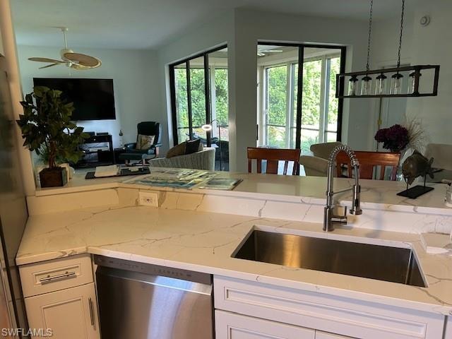 Kitchen featuring open floor plan, dishwasher, white cabinetry, light stone counters, and a ceiling fan