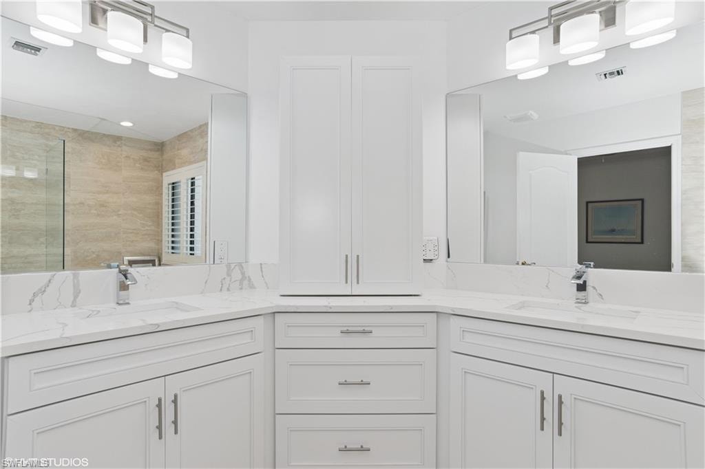 Bathroom with double vanity, visible vents, a tile shower, and a sink