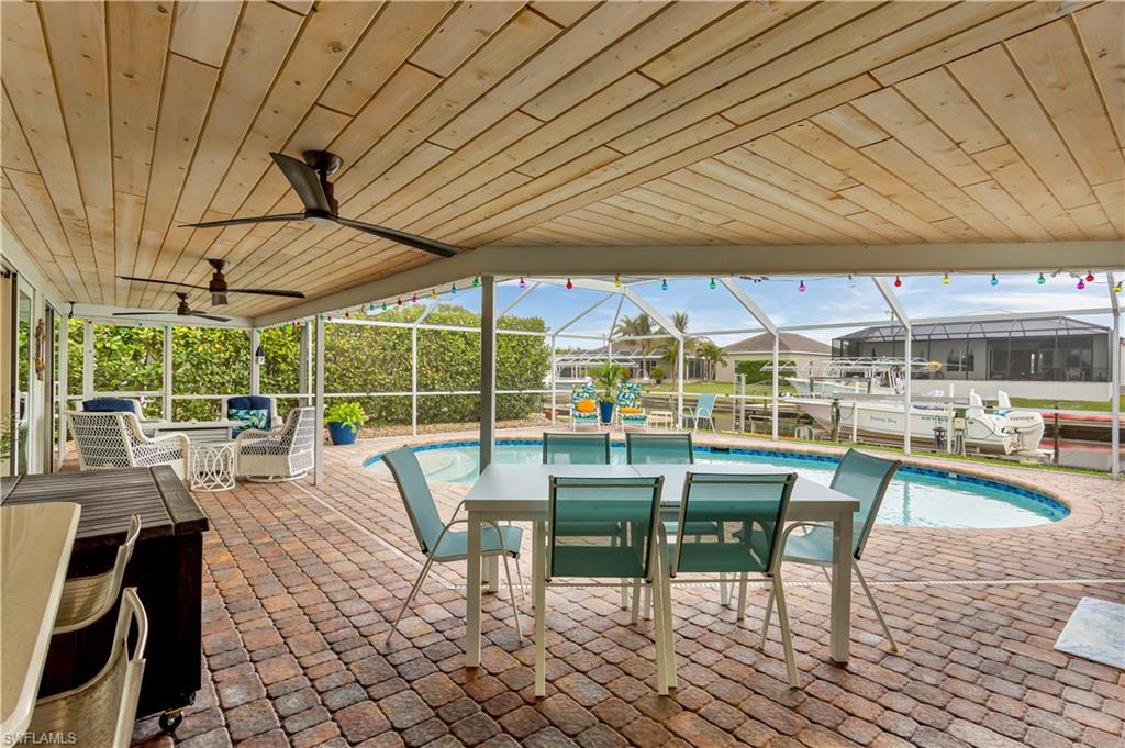View of swimming pool with screened enclosure, ceiling fan, and a patio area