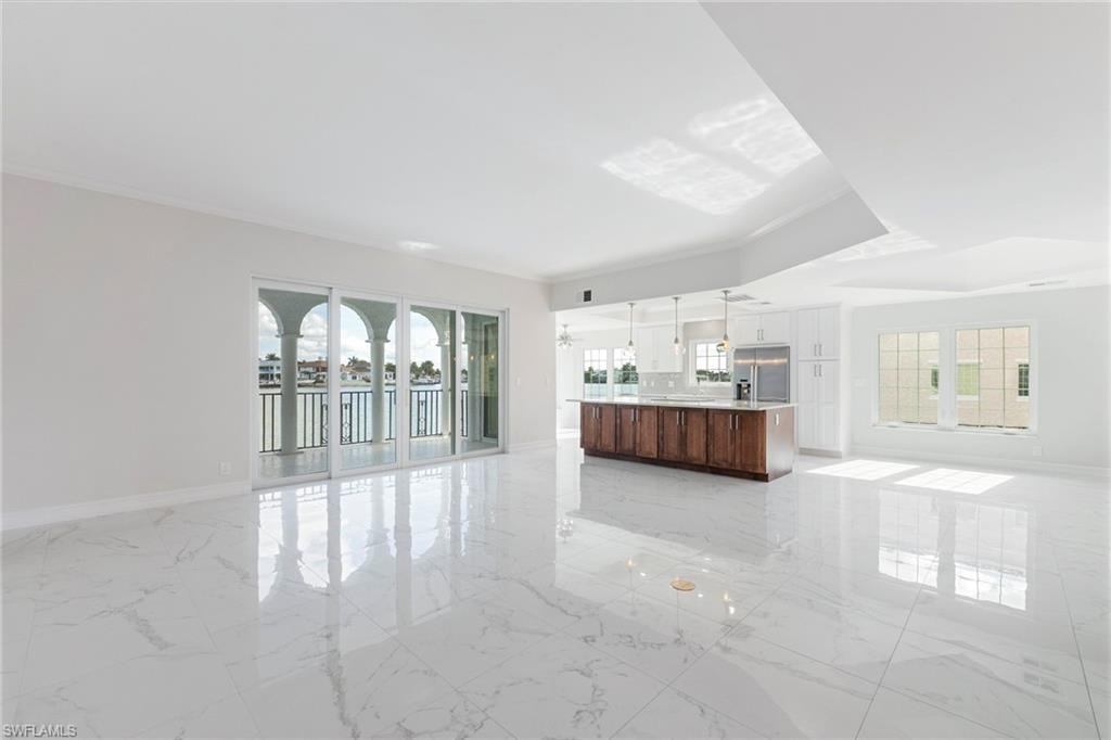 Unfurnished living room with plenty of natural light, light marble finish flooring, and crown molding