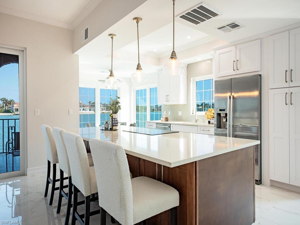 Kitchen with decorative light fixtures, a large island, white cabinetry, backsplash, and stainless steel fridge with ice dispenser
