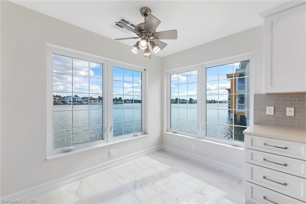 Unfurnished dining area with a water view, light marble finish floors, and a ceiling fan