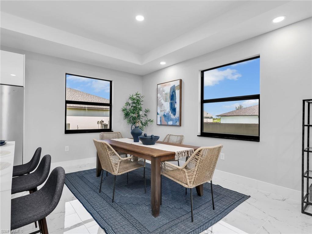Spacious dining area featuring a tray ceiling with recessed lighting, large windows with black frames, and white tiled flooring