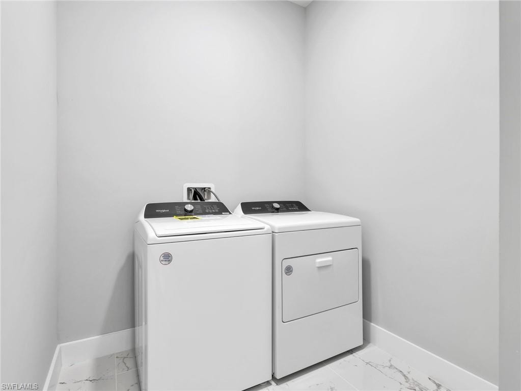 Dedicated laundry area featuring a white top-load washer, a white front-load dryer, light gray painted walls, a marble-look tile floor, and white baseboards
