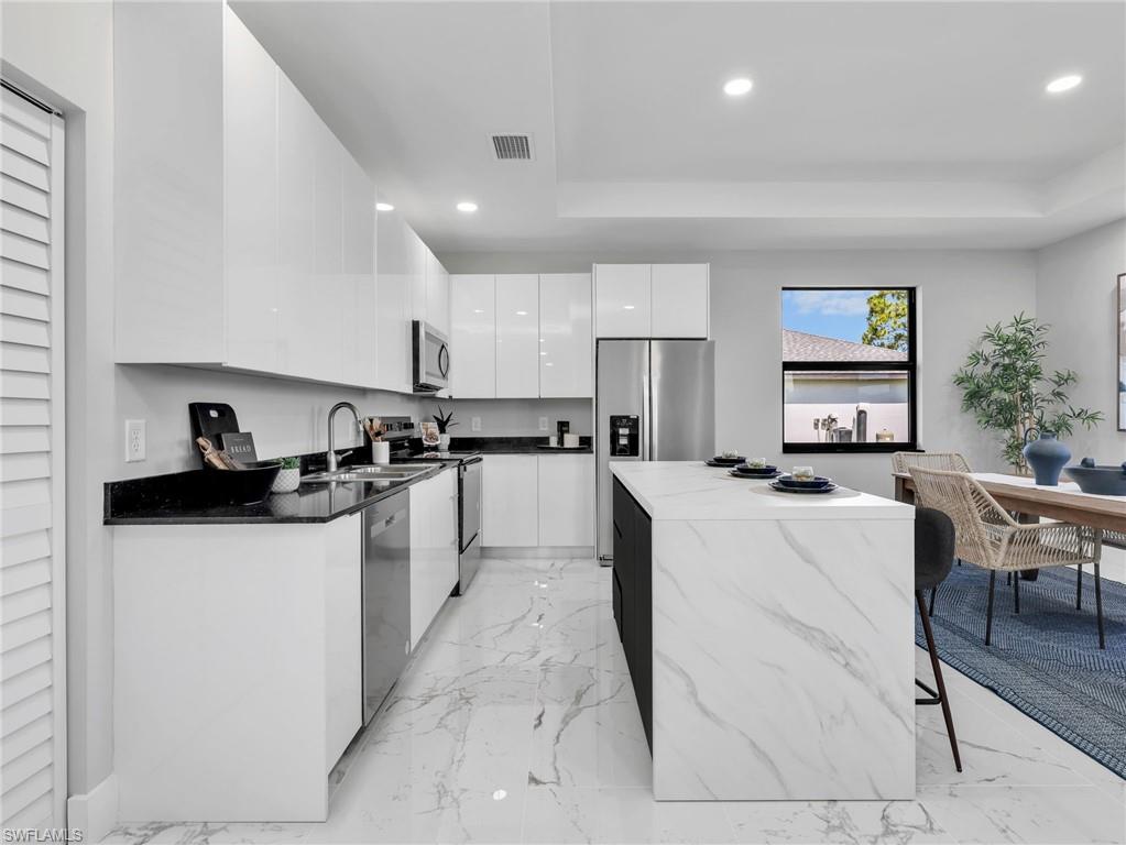 Modern kitchen featuring a waterfall island with a stone-finish countertop, high-gloss white cabinetry, black stone countertops, stainless steel appliances, and large format marble-look tile flooring
