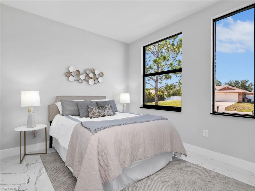 Brightly lit bedroom featuring large black-framed windows, light gray painted walls, and white marble-look tile flooring