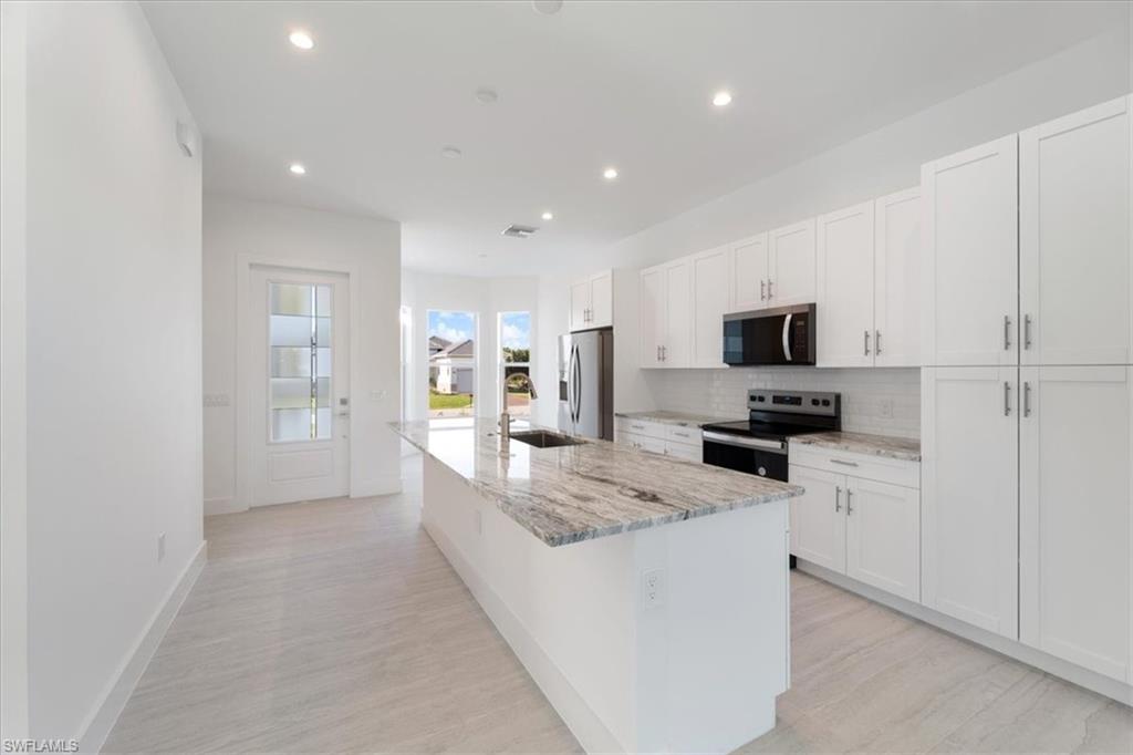 Kitchen featuring appliances with stainless steel finishes, tasteful backsplash, a center island with sink, recessed lighting, and white cabinetry