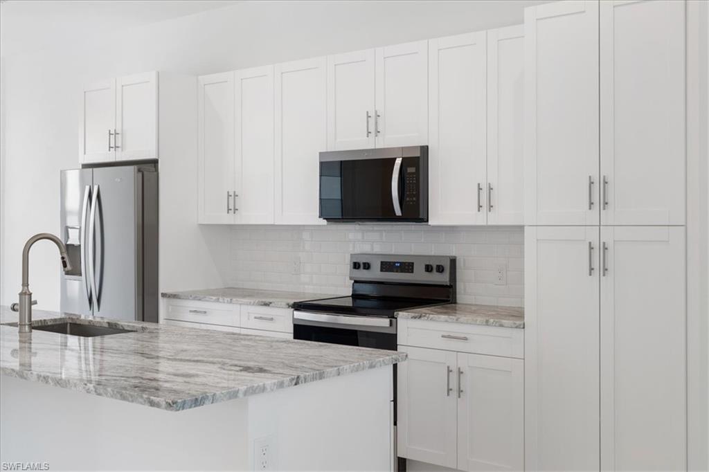 Kitchen with appliances with stainless steel finishes, tasteful backsplash, light stone countertops, a sink, and white cabinets