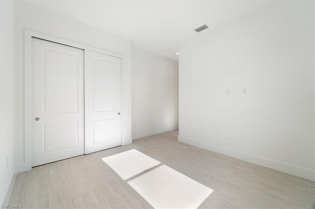 Unfurnished bedroom featuring a closet, baseboards, visible vents, and light wood-type flooring