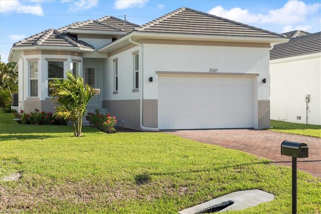 Ranch-style home with a tile roof, a front yard, decorative driveway, an attached garage, and stucco siding