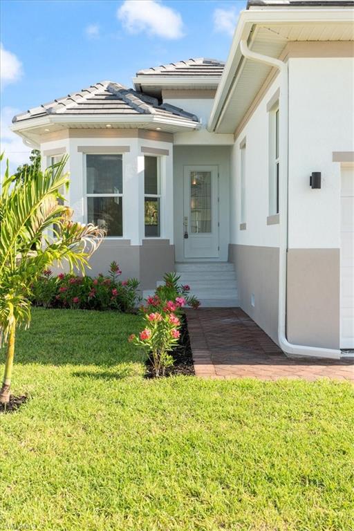 View of exterior entry featuring a tiled roof, stucco siding, and a yard