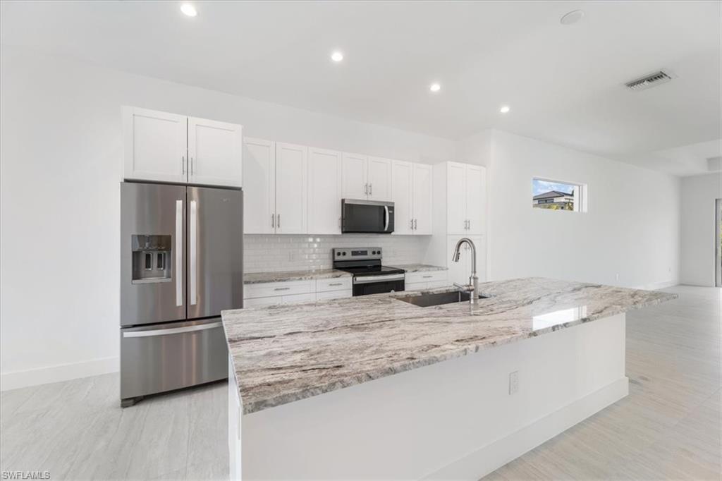 Kitchen featuring backsplash, visible vents, appliances with stainless steel finishes, a sink, and white cabinetry