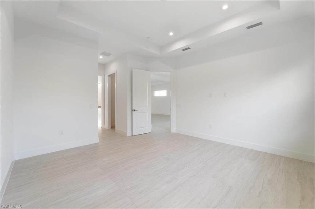 Empty room with light wood-style floors, a raised ceiling, recessed lighting, and visible vents
