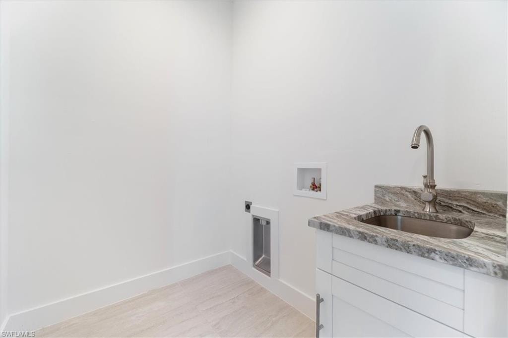 Clothes washing area featuring cabinet space, a sink, hookup for a washing machine, electric dryer hookup, and baseboards