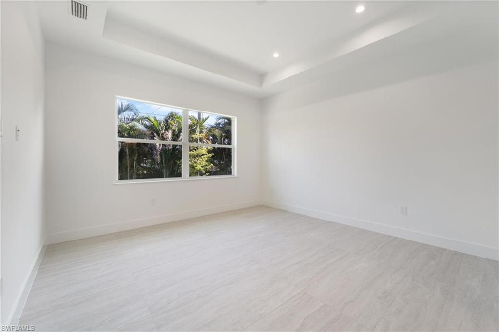 Empty room featuring recessed lighting, a tray ceiling, visible vents, and baseboards