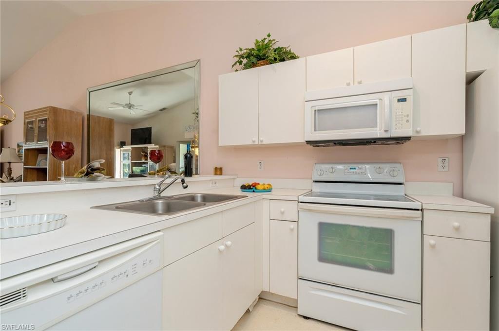 Kitchen with white cabinets, white appliances, lofted ceiling, and sink