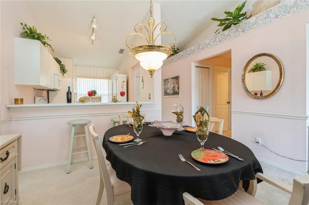 Carpeted dining room with rail lighting, vaulted ceiling, and a notable chandelier
