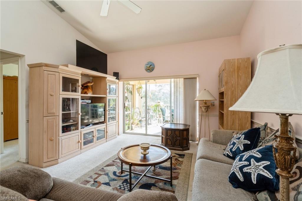 Living room with ceiling fan, light colored carpet, and vaulted ceiling