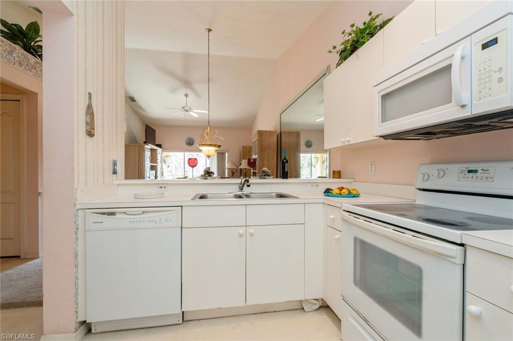 Kitchen with white appliances, ceiling fan, sink, decorative light fixtures, and white cabinetry