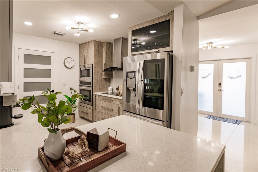 Kitchen with wall chimney exhaust hood, a chandelier, appliances with stainless steel finishes, and french doors