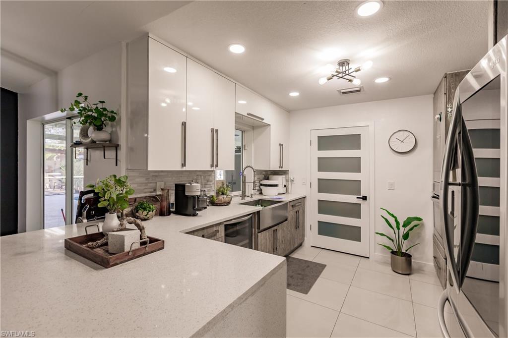 Kitchen with backsplash, sink, light tile patterned floors, white cabinetry, and stainless steel refrigerator