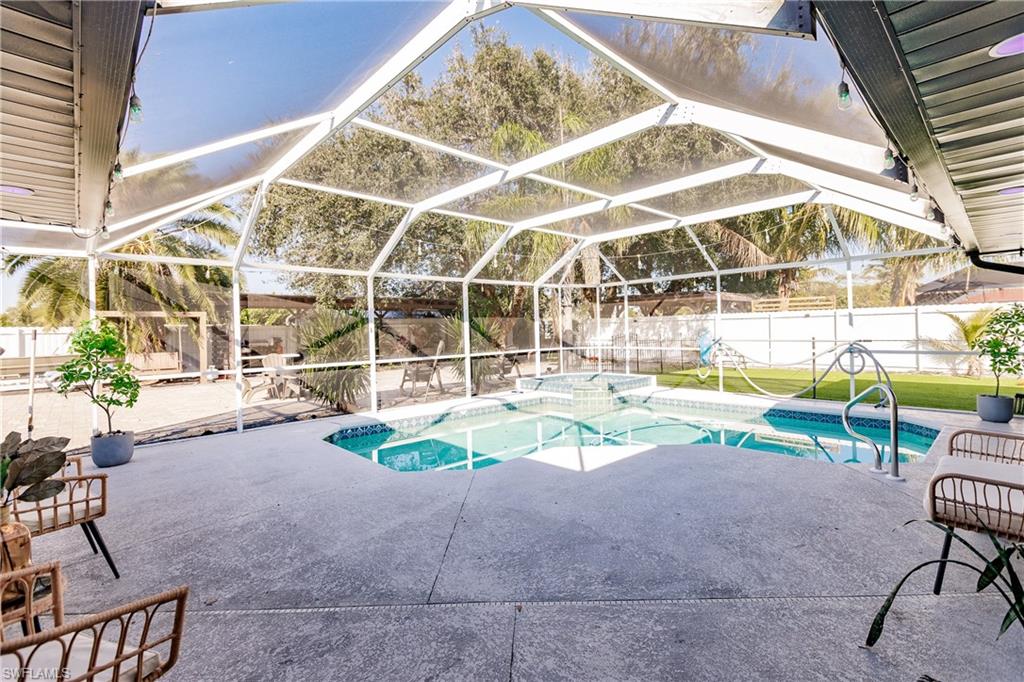 View of pool featuring glass enclosure, a patio area, and an in ground hot tub