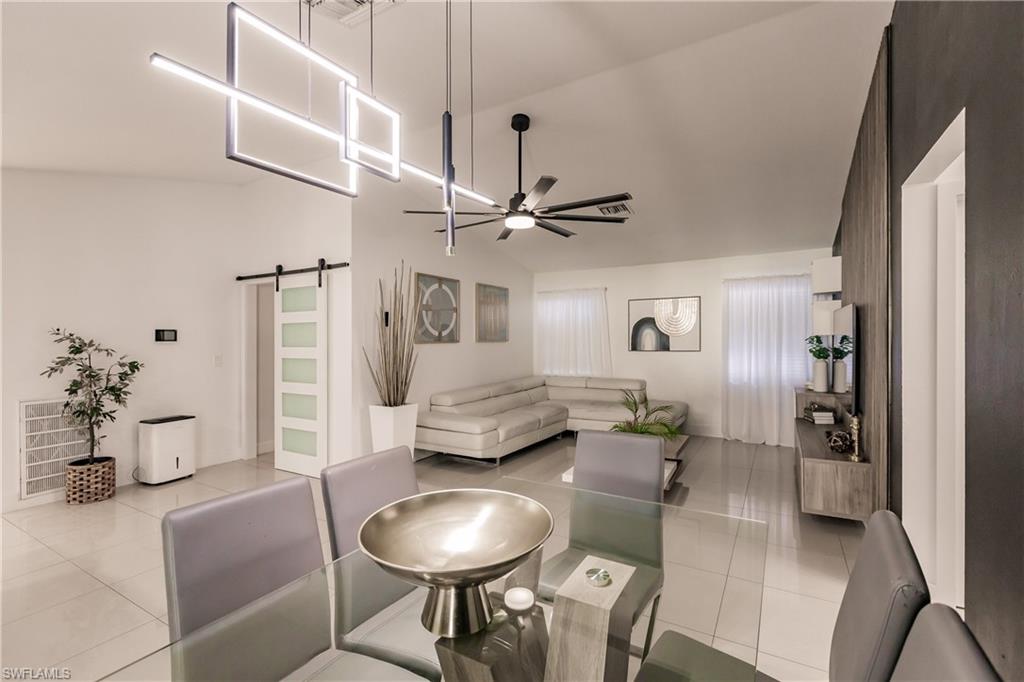 Living room with lofted ceiling, a barn door, light tile patterned floors, and ceiling fan