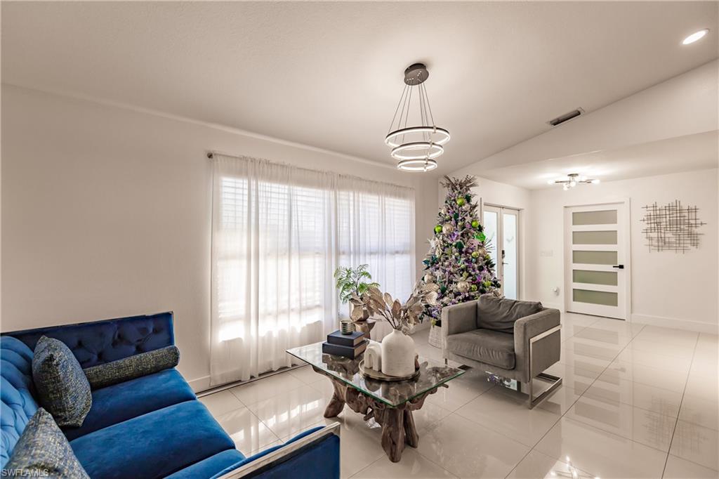 Living room featuring light tile patterned floors, lofted ceiling, and a notable chandelier