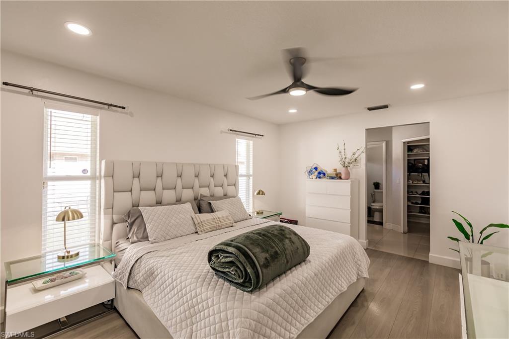 Bedroom with a spacious closet, ceiling fan, wood-type flooring, and multiple windows