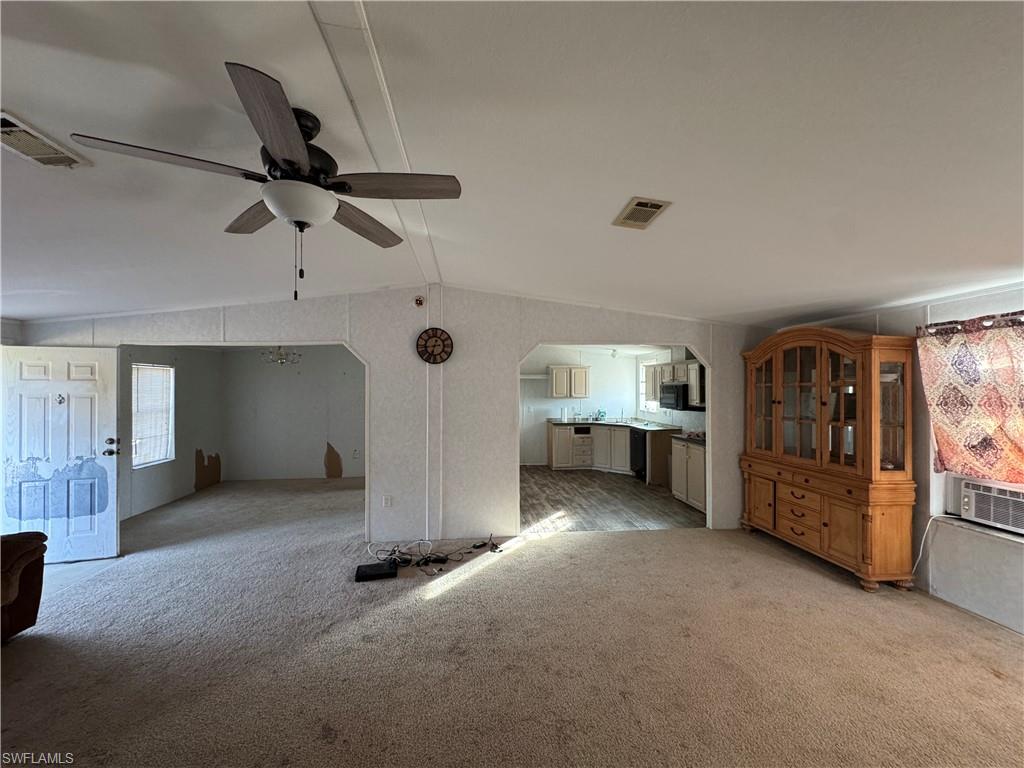 Unfurnished living room with light colored carpet, ceiling fan, and lofted ceiling