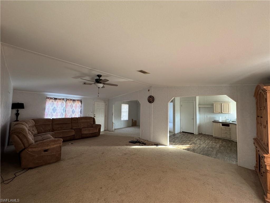 Unfurnished living room with light colored carpet, ceiling fan, and lofted ceiling