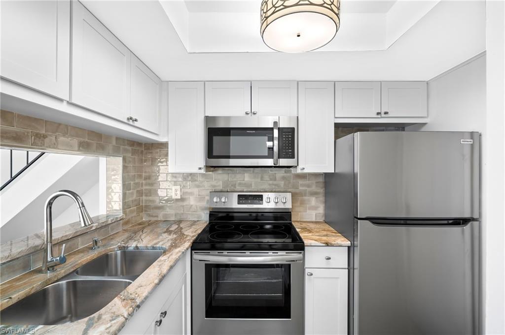 Kitchen featuring light stone counters, white cabinetry, sink, and appliances with stainless steel finishes
