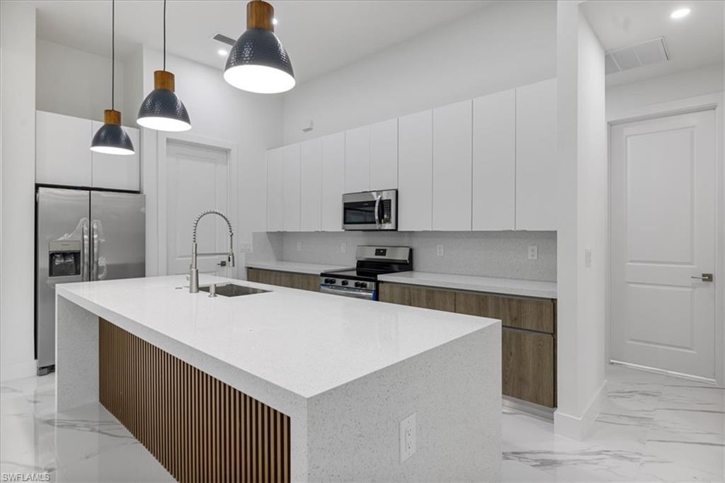 Kitchen featuring white cabinets, decorative light fixtures, stainless steel appliances, and an island with sink