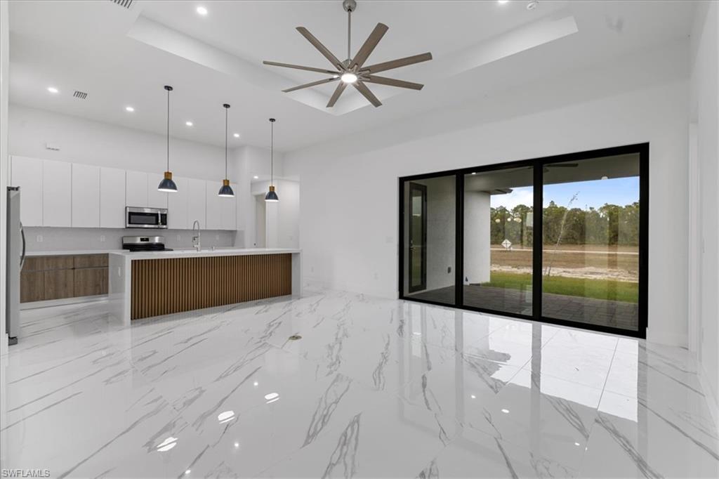 Kitchen with a raised ceiling, an island with sink, white cabinets, and stainless steel appliances