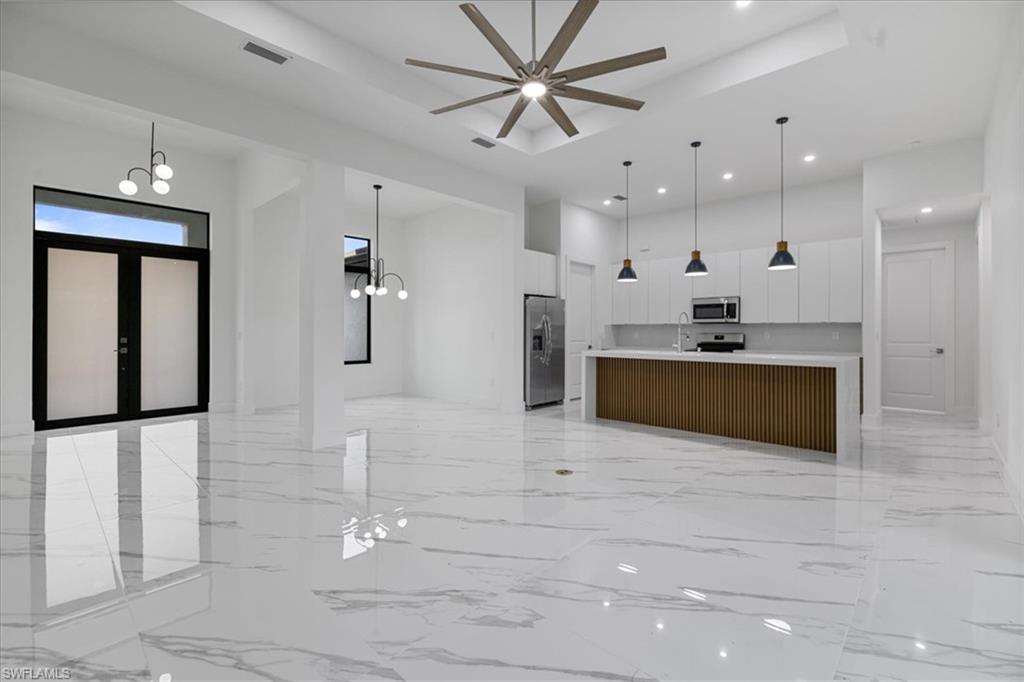 Kitchen with pendant lighting, a large island with sink, sink, white cabinetry, and stainless steel appliances