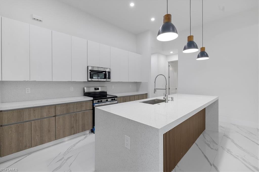 Kitchen with pendant lighting, a kitchen island with sink, sink, white cabinetry, and stainless steel appliances