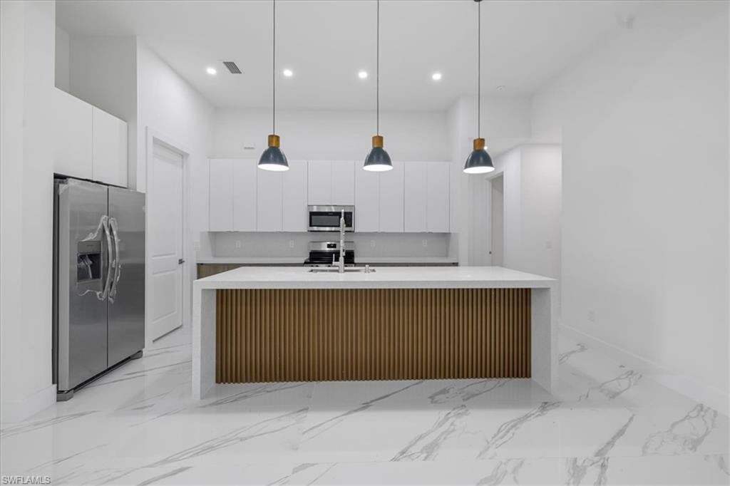 Kitchen with a center island with sink, white cabinets, stainless steel appliances, and hanging light fixtures