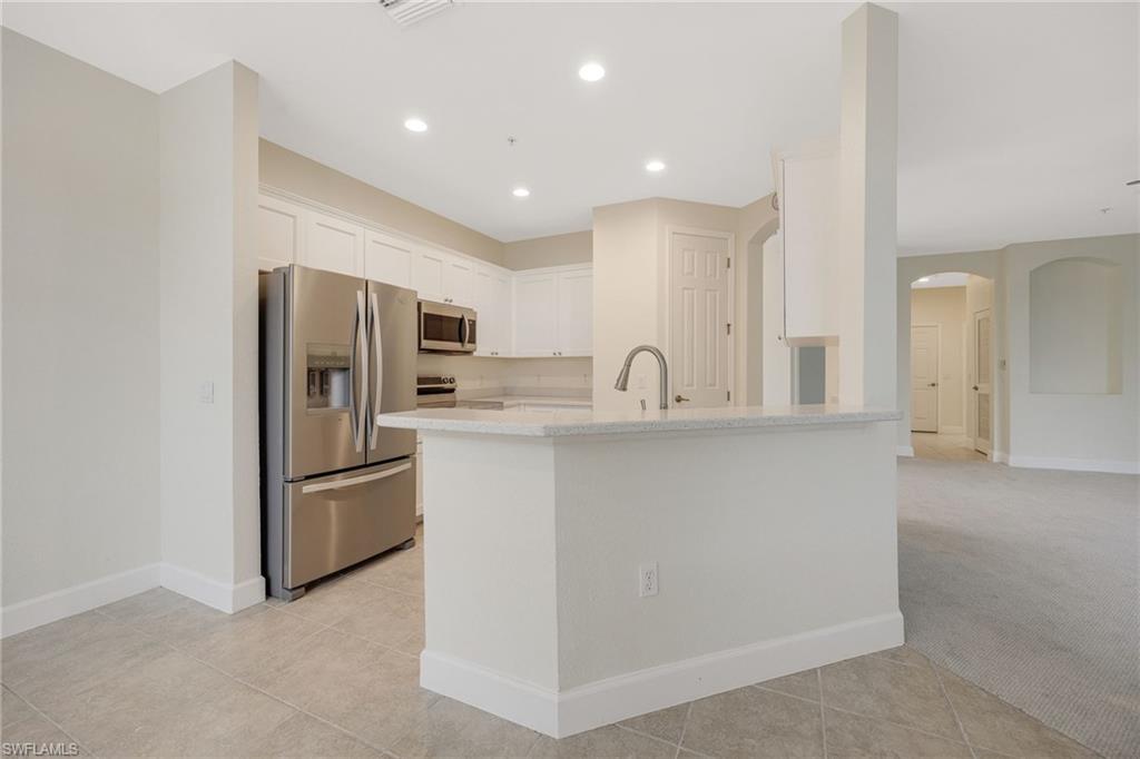 Kitchen featuring white cabinetry, sink, light colored carpet, stainless steel appliances, and light stone counters