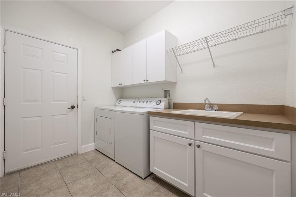 Laundry area with sink, cabinets, washer and dryer, and light tile patterned floors