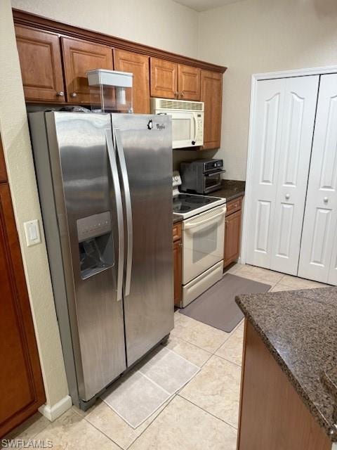Kitchen featuring dark stone counters, stainless steel fridge, light tile patterned floors, and stove