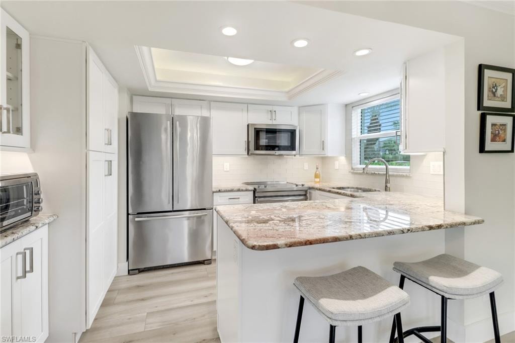 Kitchen featuring sink, white cabinets, a raised ceiling, and stainless steel appliances