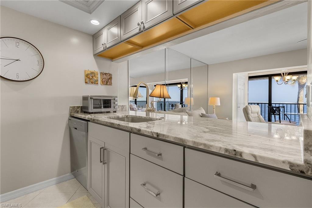 Kitchen featuring sink, stainless steel dishwasher, light stone countertops, and gray cabinets