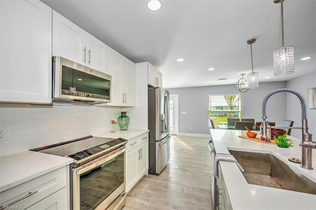 Kitchen with sink, decorative light fixtures, white cabinets, light wood-type flooring, and appliances with stainless steel finishes