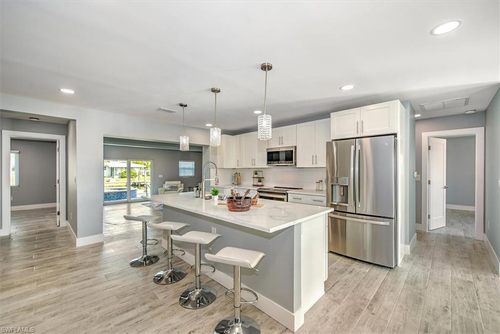 Kitchen featuring a kitchen breakfast bar, stainless steel appliances, an island with sink, pendant lighting, and white cabinets