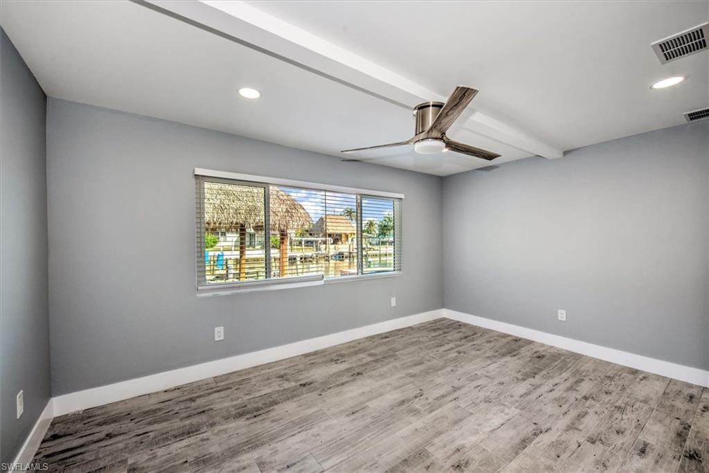 Empty room with beam ceiling, ceiling fan, and wood-type flooring