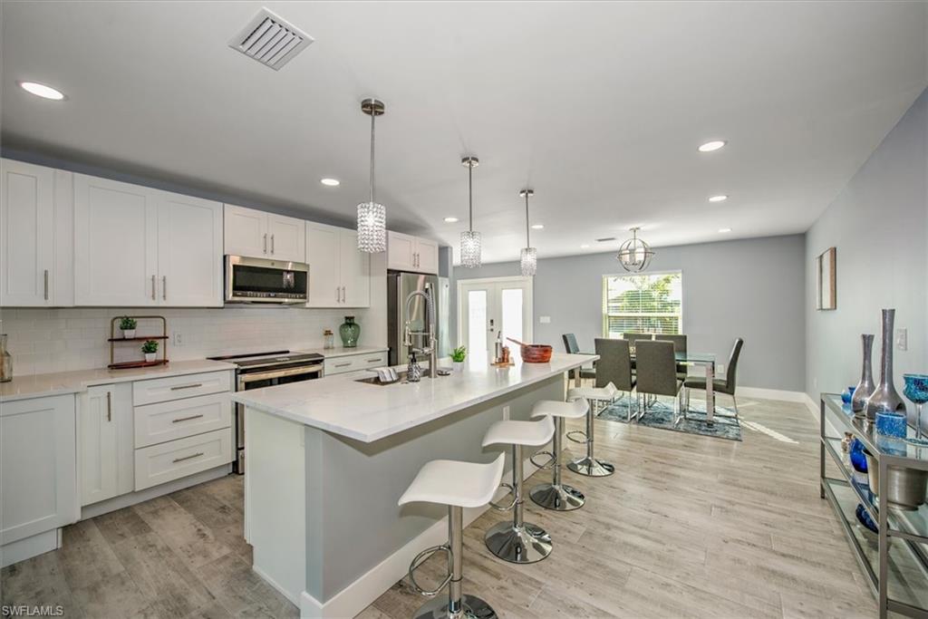 Kitchen with a center island with sink, decorative light fixtures, white cabinetry, and appliances with stainless steel finishes